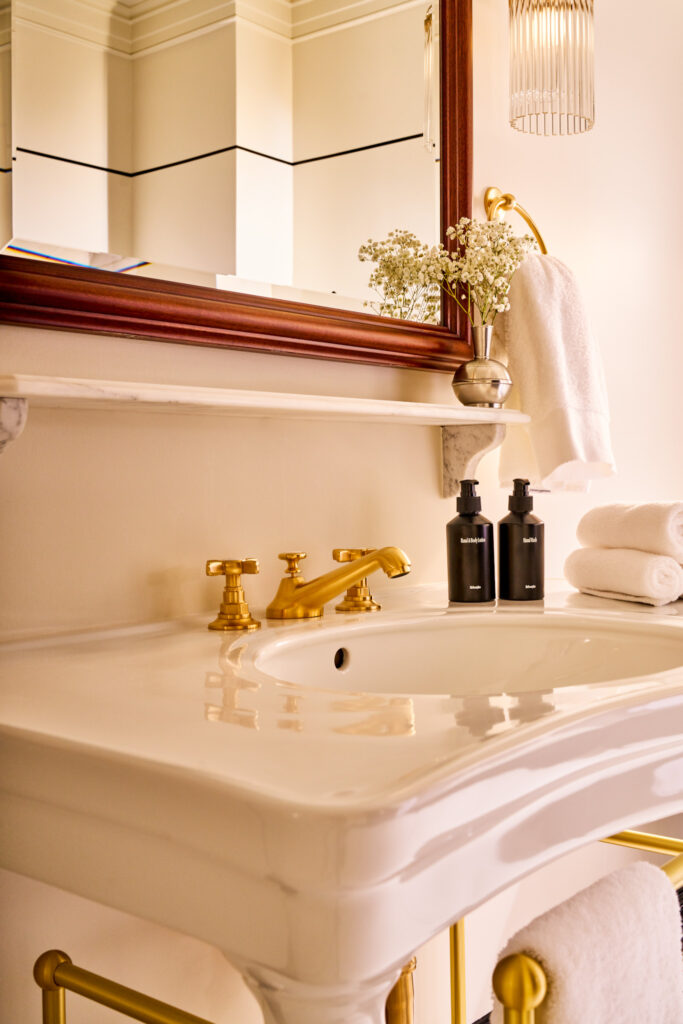 Bathroom sink and mirror at The Twenty Two New York, featuring a gold-colored faucet and elegant design details.